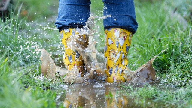 Child splashing in puddle with colorful rain boots. - Powered by Adobe