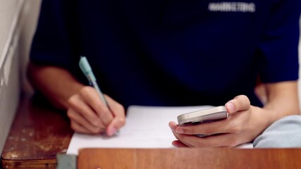 Smartphone in student hand placed above exam papers and pen on classroom desk, showing distraction or digital support in test. - Powered by Adobe