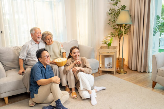 Happy Asian family senior parents and adult child spending time together at home. Elderly father and mother watching movie on tv with daughter and son in living room. Aged people mental healthcare. - Powered by Adobe