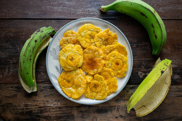 Delicious patacones on a plate with green plantains on rustic wooden table