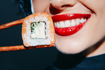 Fototapeta na wymiar Young woman with red lips smiling while holding sushi with chopsticks, showcasing vibrant colors and a modern dining concept.