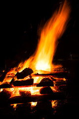 Narrow focus of a crackling bonfire at night in Brazil. Orange flames dance among stacked wood,...