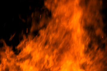 Narrow focus of a crackling bonfire at night in Brazil. Orange flames dance among stacked wood,...