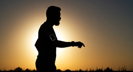 Silhouette of a man jogging with smartphone and smartwatch against golden sky