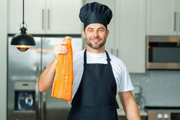 Man chef cooker hold fish salmon. Male chef in chefs uniform with raw fish salmon fillet. Chef man...