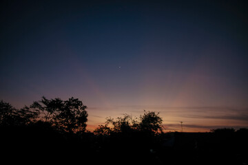 Crescent Moon in Twilight Sky with Silhouetted Trees at Sunset