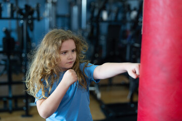 Kid punching a boxing bag. Kid boxer boxing in gym. Child wearing boxing gloves. Boy practicing martial arts. Kid fighter portrait. Sporty kid, active child doing boxing. Healthy boy exercising power.