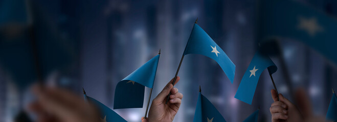 Somalia flags in their hands on a blurred urban background