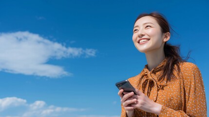 Young Asian woman smiling while holding cellphone and looking at blue sky,copy space,banner.