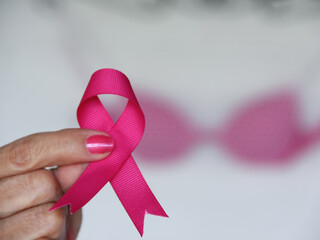 Selective focus of woman holding pink ribbon with pink bra in the background for Brest Cancer Awareness Month concept in October. 