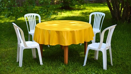 Round table with yellow tablecloth and chairs in garden