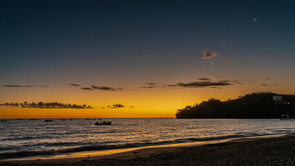 Evening after sunset. Tropical twilight. The blue sky is highlighted orange near the horizon. Beautiful clouds. Silhouettes of boats in the ocean. Waves are foaming on a sandy beach. Madagascar.