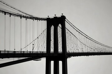 Fototapeta premium Monochrome artistic photo of suspension bridge with steel cables spanning across water with city backdrop 