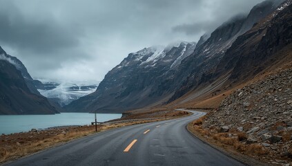 Winding mountain road along a glacial lake with dramatic rocky cliffs under overcast skies