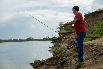 Fototapeta premium Grandfather is teaching a grandson fishing on the river beach.