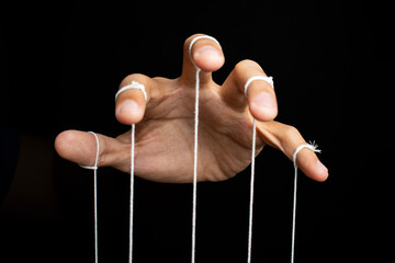 male puppeteer hand with strings isolated on black background. manipulation or controlling concept