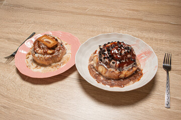 Two different fresh cinnamon buns served on a wooden table