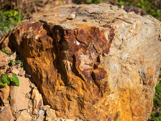 Close-up of large sandstone rock with rough texture and natural orange-brown surface details in sunlight.