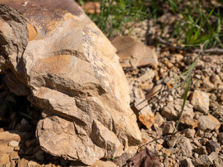 Close-up of a sandstone rock fragment with rough surface and sharp edges lying on dry ground with small stones