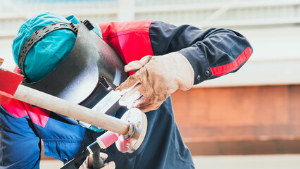 A skilled welder focuses intently while working on metal pipes in a well-lit industrial workshop....