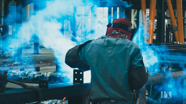 A dedicated welder focuses on detailed metal fabrication in a vibrant industrial workshop. Smoke and sparks fill the air as tools are expertly used to shape materials
