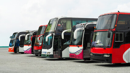 Several buses of different colors are lined up at a transportation hub, ready for passengers. The cloudy sky adds a moody backdrop to this bustling urban setting © Happy Photo