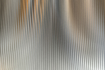 Obraz premium A textured metallic surface with vertical ribbed patterns and subtle hints of warm orange light reflecting on the corrugated metal
