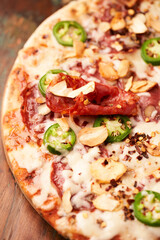 Pizza with salami, mozzarella cheese and jalapeno pepper. Wooden background. Soft focus.