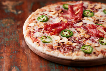 Pizza with salami, mozzarella cheese and jalapeno pepper. Wooden background. Soft focus.