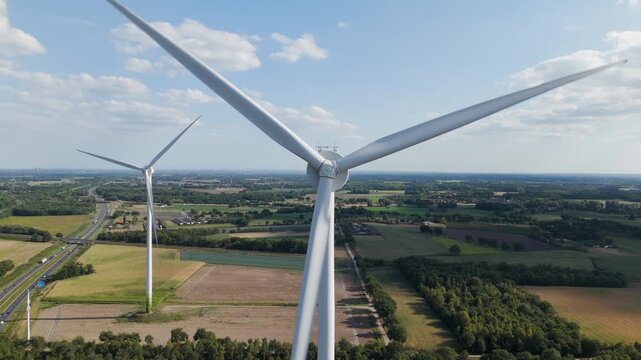Aerial drone close-up of wind turbine blades spinning under bright blue sky.