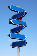 Multiple blank blue arrow signs pointing in various directions against a clear blue sky, symbolizing choices and future paths.