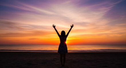 A woman standing on a beach with her arms raised, enjoying the sunset.