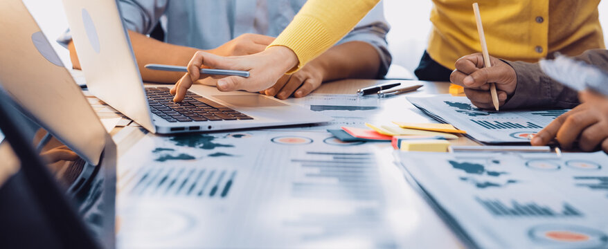 Engaging business meeting showcasing professionals collaborating over charts and statistics, utilizing laptops and stationery in a bright, modern office environment. SACTR