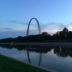 Twilight view of iconic arch reflected in calm water, city skyline in background