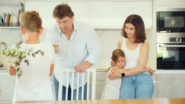 Preteen boy being scolded by angry parents in the kitchen, little sister watching him with empathy. High quality 4k footage