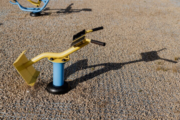 Outdoor ab crunch fitness machine on gravel surface, yellow and blue exercise equipment in a public...