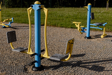 Outdoor seated shoulder press and leg push fitness machine in a public park, colorful exercise...