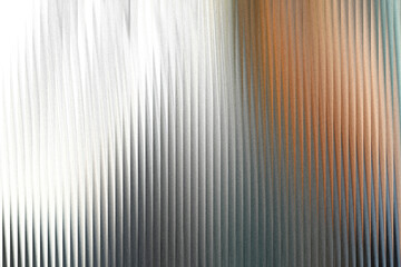 Obraz premium A textured surface with vertical ridges, transitioning from bright white and silver on the left to warm brown and cool blue tones on the right, creating a visually dynamic abstract background