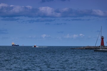 Obraz premium Ships navigate calm waters near harbor under a blue sky with clouds during daylight