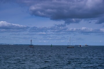 Sailboats on a calm ocean under cloudy skies near a coastal town in the afternoon