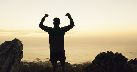 Silhouette, man and winning with fist pump on mountain for conquer, achievement or accomplishment. Active, male person or back view with sunset in celebration for hiking success or milestone on space