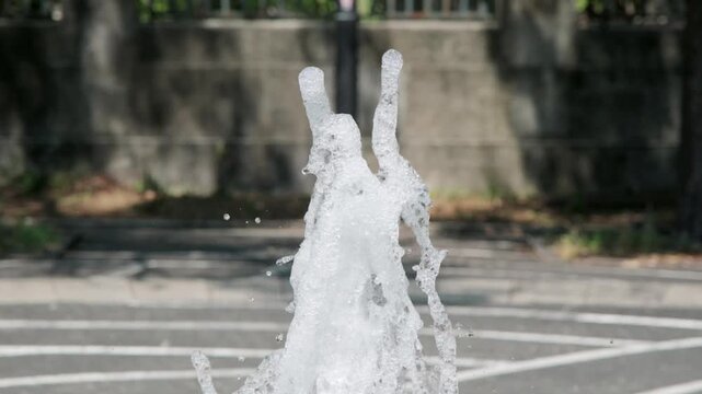 吹きあがる公園の噴水の水しぶき　夏の街の風景　暑い日差しを受けて風に煽られる水滴