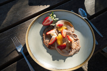 Buckwheat pancakes with fruit slices on a plate on a wooden table