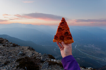 Women holds slice of pizza on mountain top at sunset