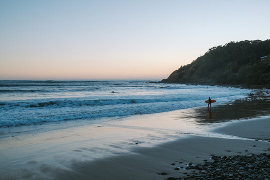 Surfer holding surfboard walking on beach at sunset