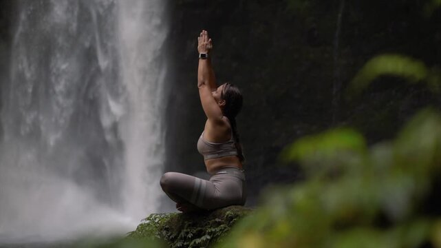 Woman practicing yoga in front of Nungnung waterfall in lush jungle