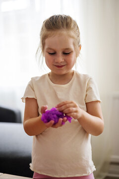 Little girl holding playing with purple slime putty at home