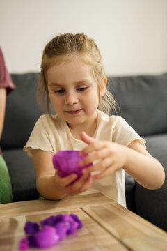 Little girl holding playing with purple slime putty at home