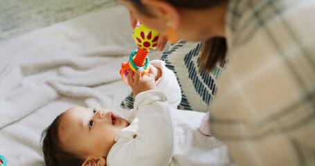 Hands, baby and play with rattle in nursery, mother and stimulation with color, sound and happy in home. People, mom and infant child with toys, game or bonding on bed for development in family house