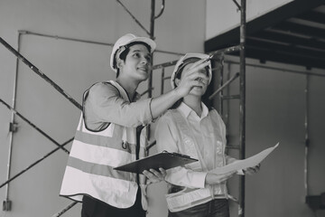 Construction manager and engineer dressed in orange work vests and hard helmets explore construction documentation on the building site near the steel frames